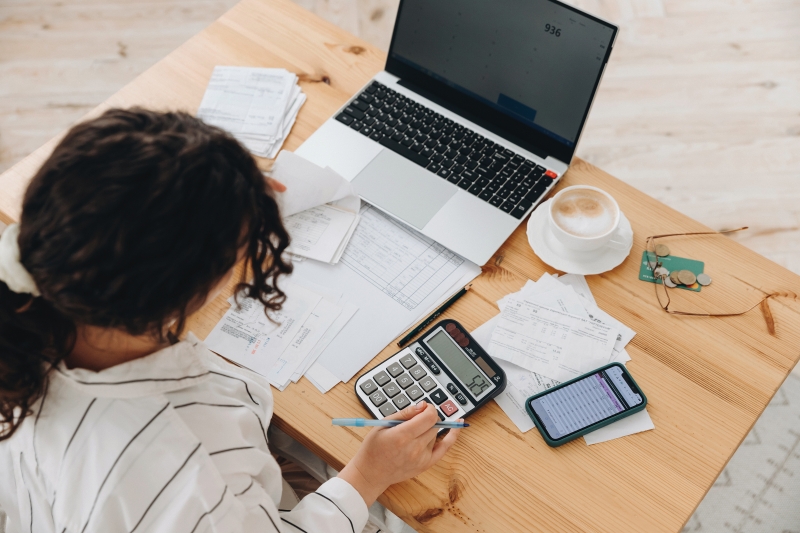 Top view of student working at laptop with calculator, bills, and coffee.