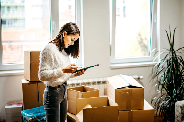 Woman looks at a tablet while standing beside moving boxes