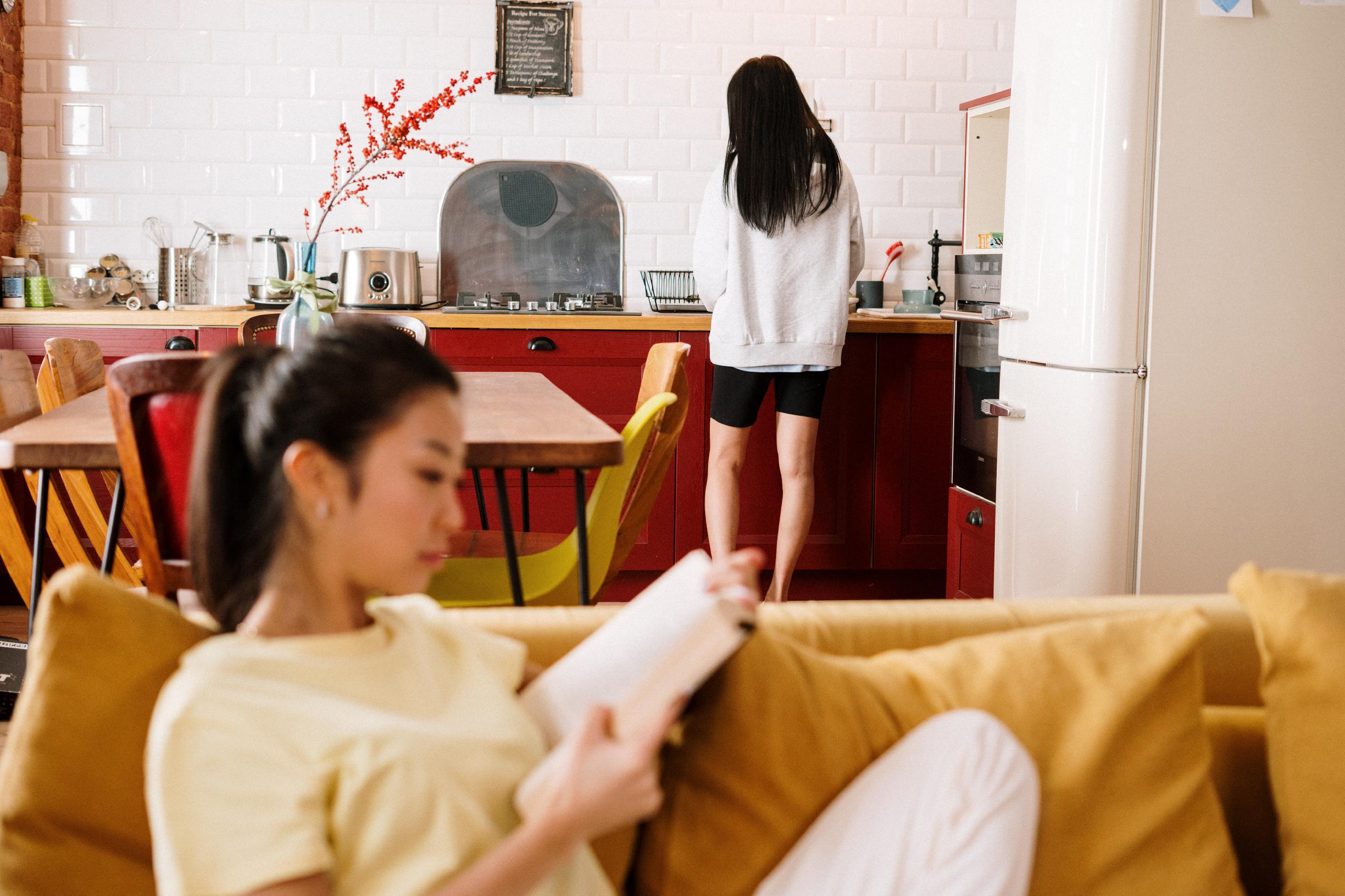 Image of one roommate reading while the other roommate washes dishes
