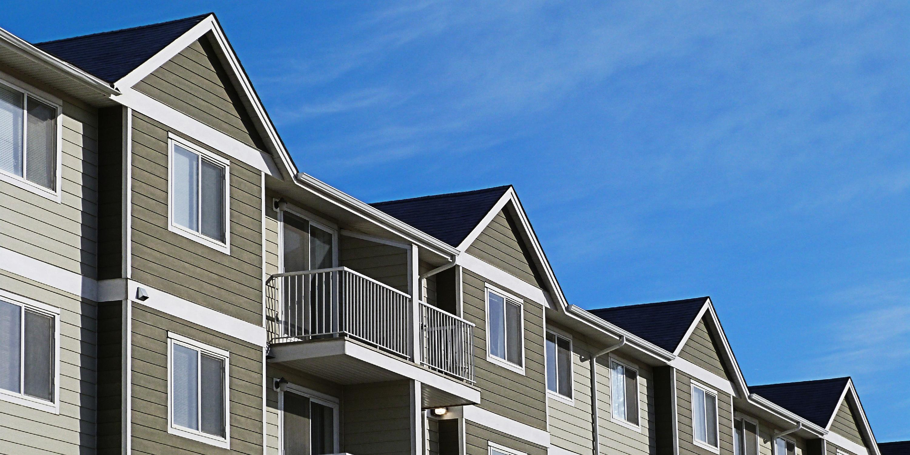 Rooftops of a row of townhomes against a clear blue sky.