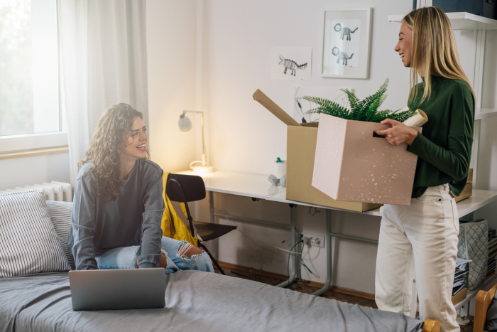 Two students laugh while unpacking moving boxes in an apartment.