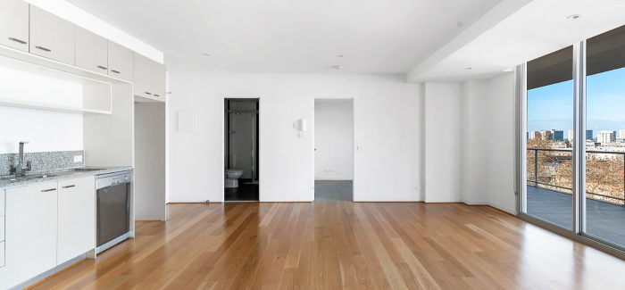 Bright, empty studio apartment living space with hardwood floors.