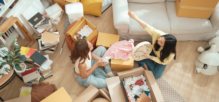 Two roommates unpacking boxes on the floor ofa bright apartment.
