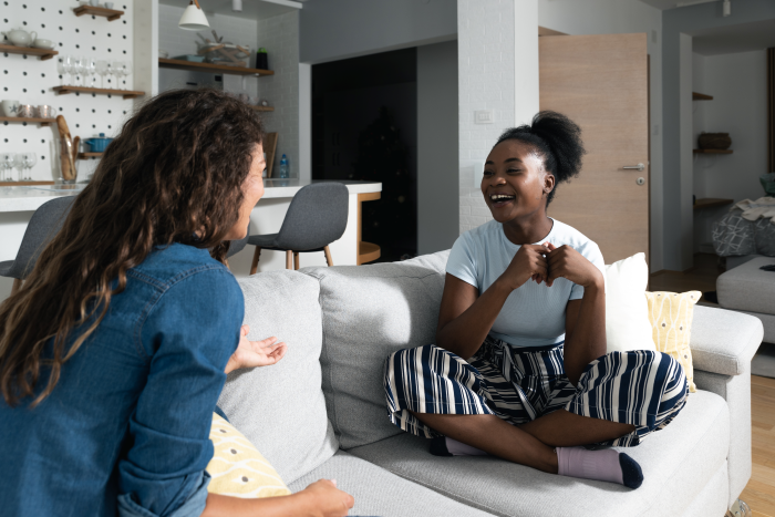 Two young women chatting and laughing on a couch.