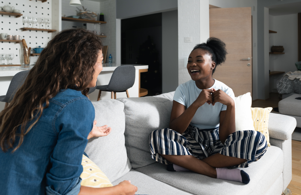 Two students seated on a couch talking and laughing.