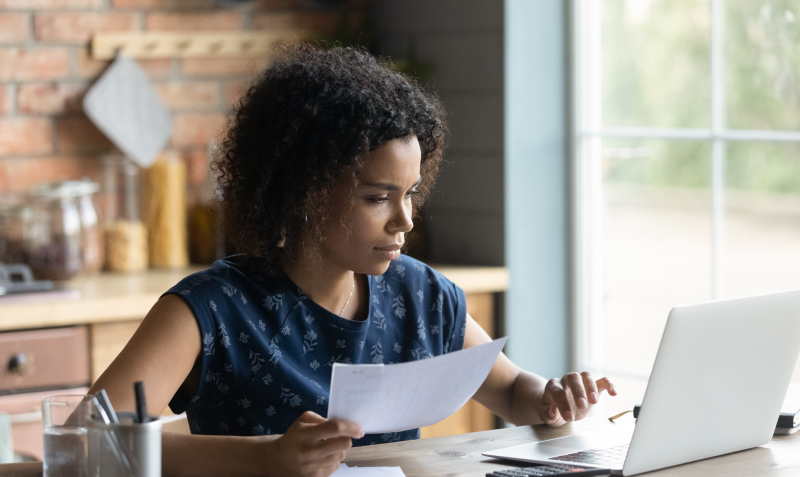 Student working on a laptop with a sheet of paper.