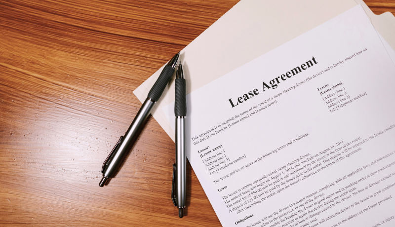 Pens and a printed lease agreement lying on a wooden table.