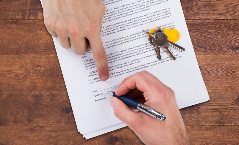 Close-up of a document being signed, with keys placed on top.