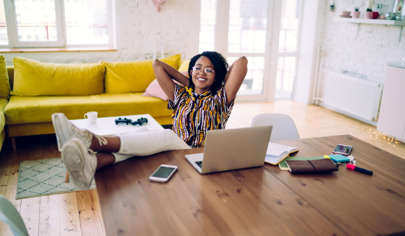 Student sitting at home with their feet propped up on table looking at their laptop.