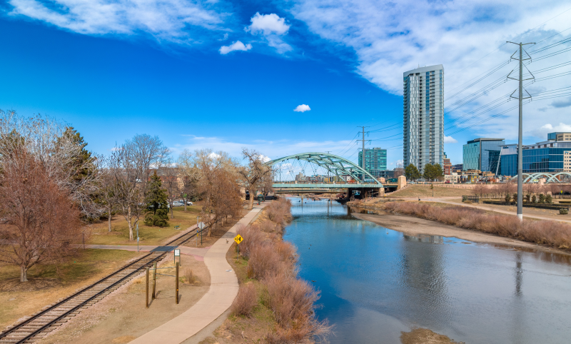 River in Auraria running next to power lines with view of bridge and skyscrapers in the background.
