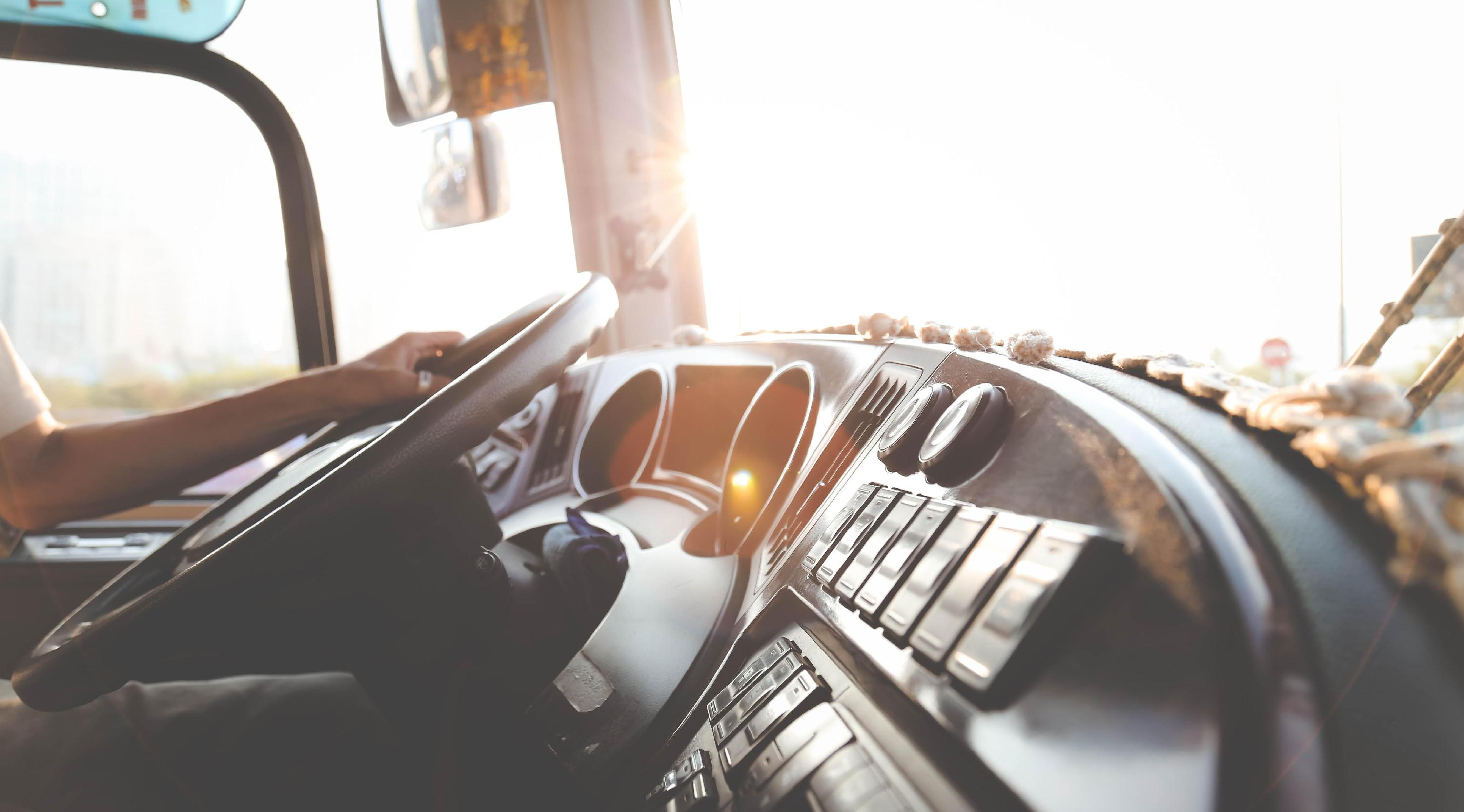 Bus driver’s hands on the steering wheel in sunlight.