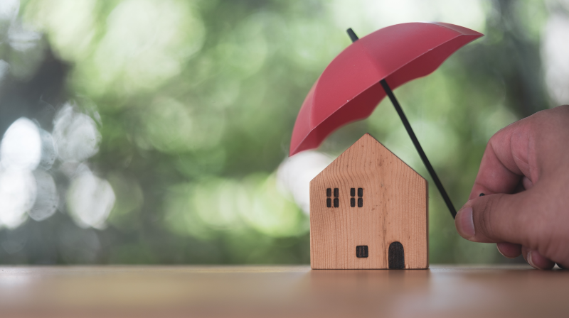 Small house figurine protected by a tiny umbrella