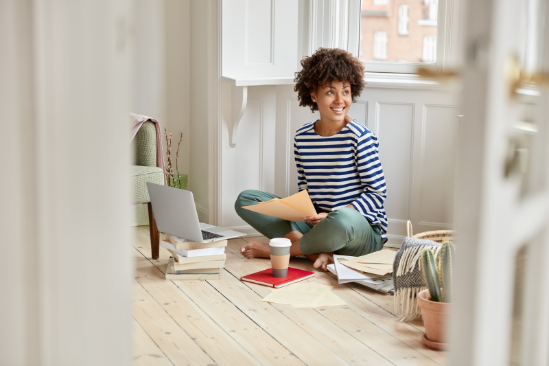 Student sitting on the floor of a bright apartment with laptop and coffee.