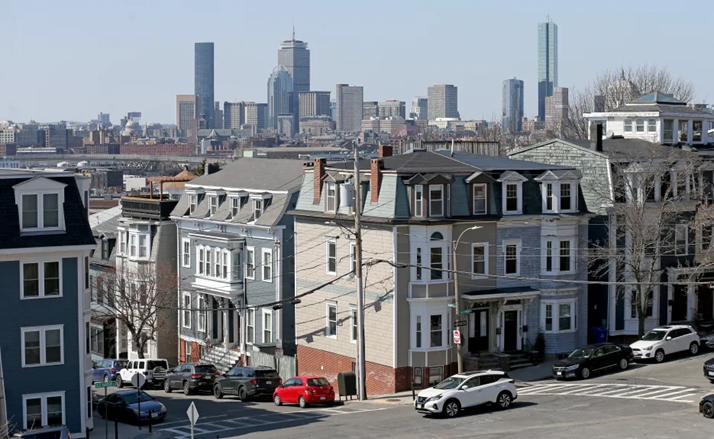 Boston rowhomes under a blue sky with skyscrapers in the background.