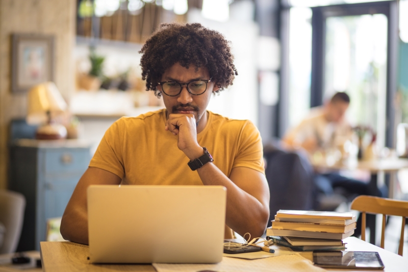 Student seated at a table concentrating on laptop.